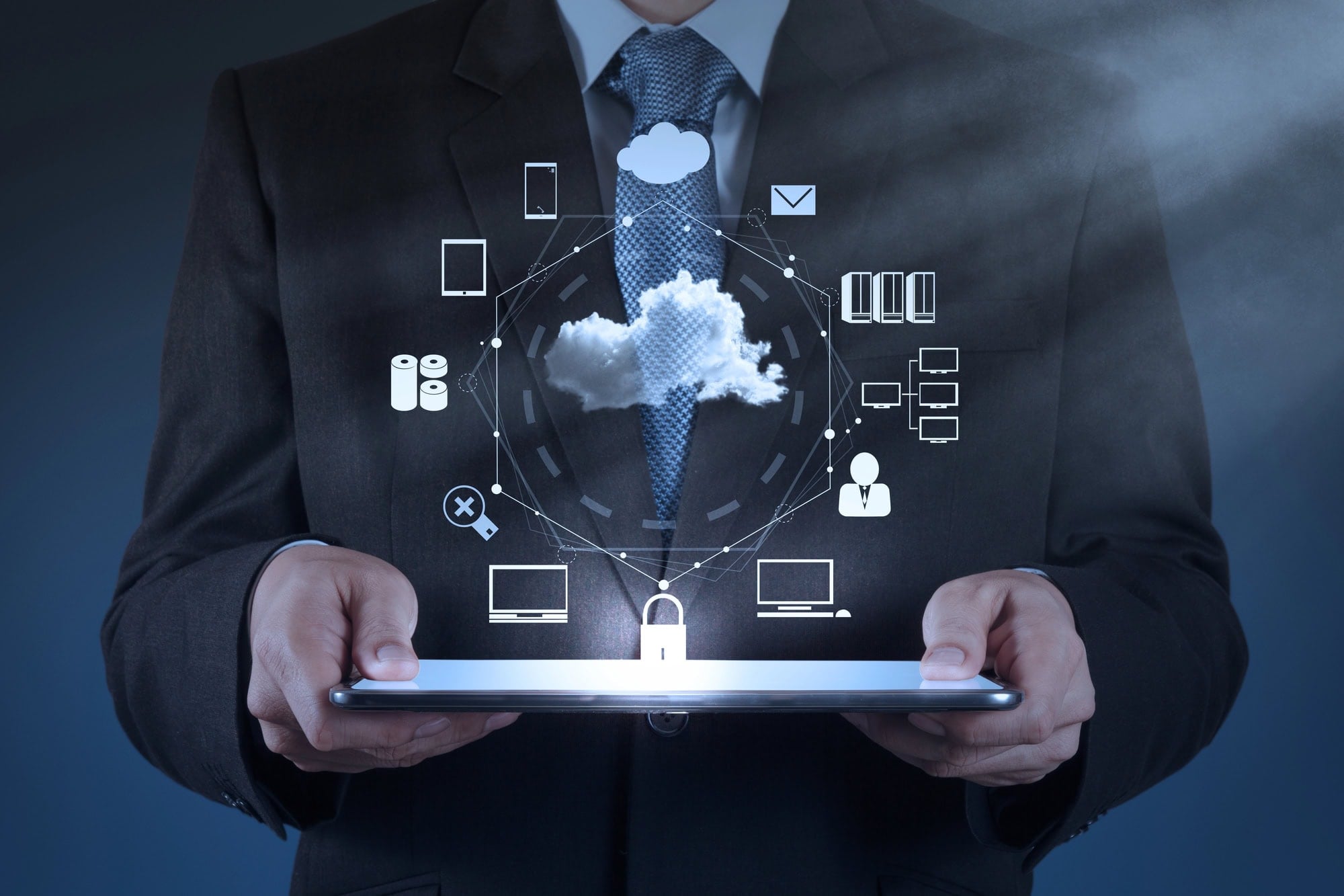 A person in a suit holds a tablet with floating cloud computing icons above it, representing data storage, security, and…