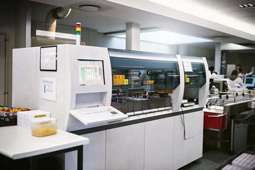 Large automated laboratory machine processes test samples in a modern, brightly lit lab.